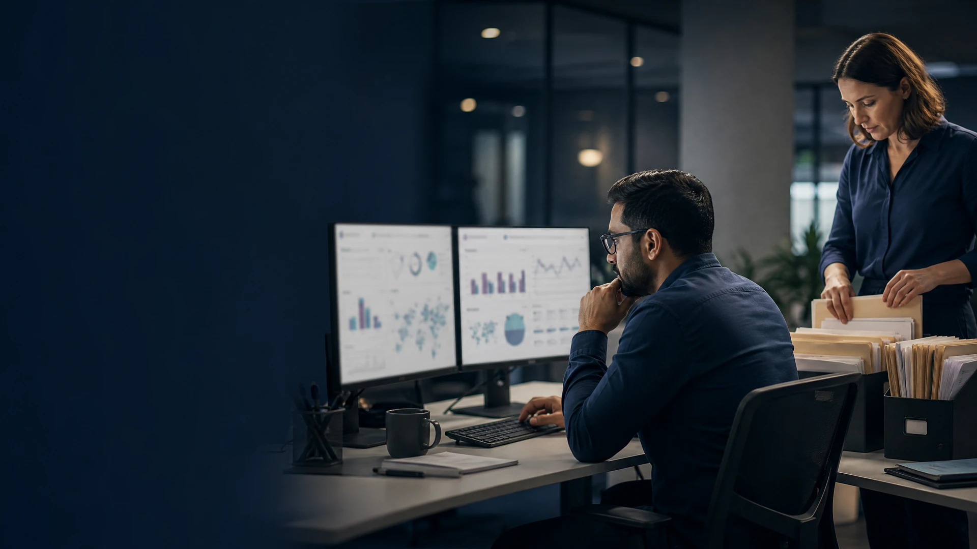 Operations analyst examining data dashboards while a colleague organizes records.